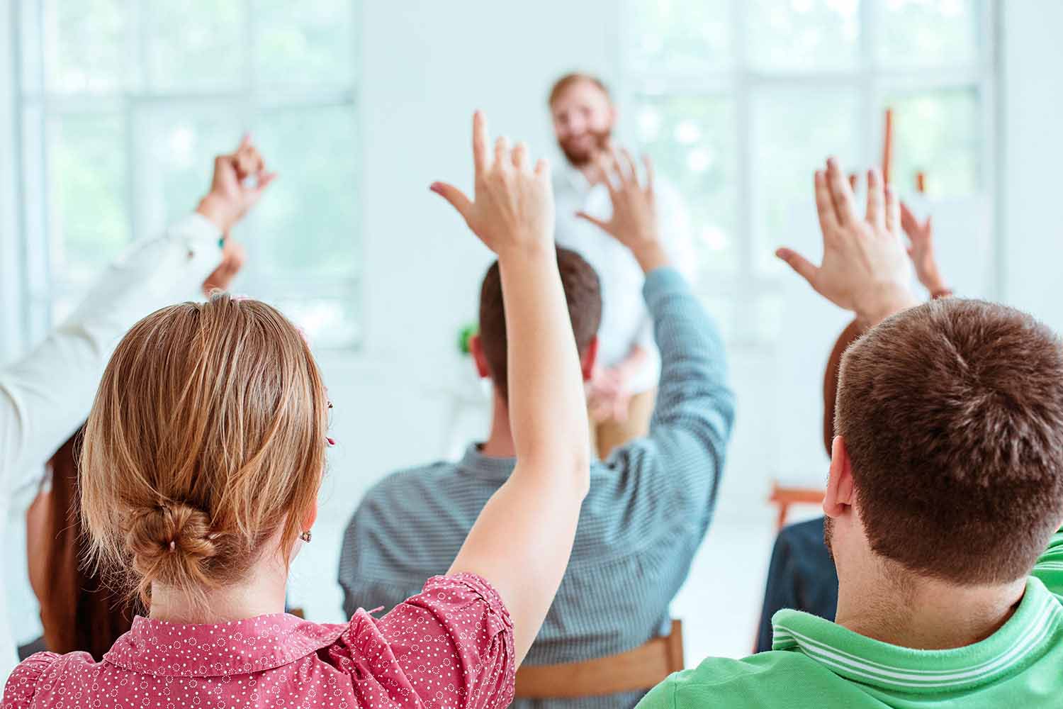 İçeride sırtları kameraya dönük olarak oturan bir grup insan ellerini, odanın önünde gülümseyerek akredite sertifika ve sürdürülebilirlik gibi konularda dinleyicilerle sohbet eden TÜV Austria Türk konuşmacısına doğru kaldırıyor.